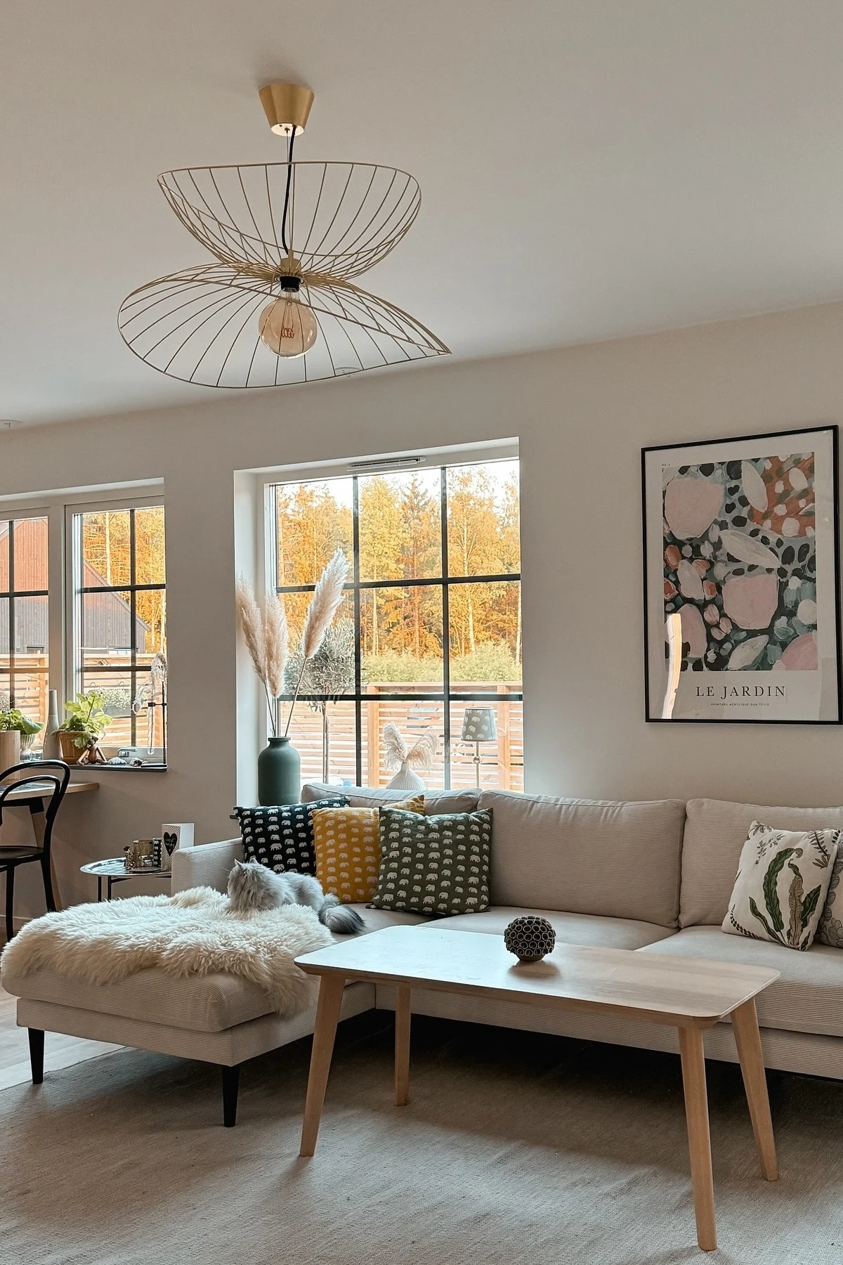 In einem fröhlichen skandinavischen Wohnzimmer mit Couch, Couchtisch und großen Fenstern, hängt die Ray-Deckenleuchte von Globen Lighting.