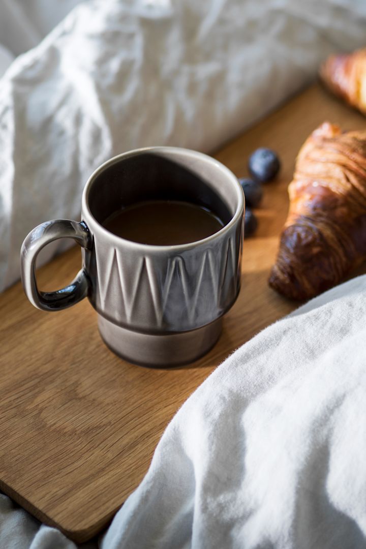 Die Coffee & More Espressotasse in Grau steht auf einem Holzbrett in einem Bett, daneben ein Croissant.
