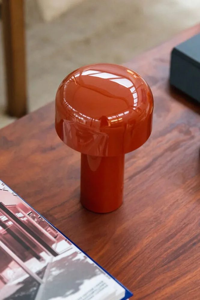 Glänzende orangefarbene Pilzlampe auf einem Holztisch, mit einem Magazin im Vordergrund.