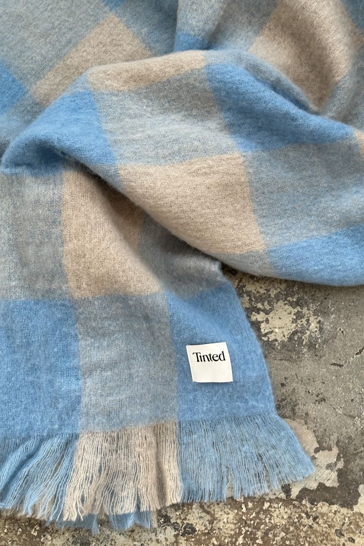 Hier sehen Sie eine blau-beige karierte Wolldecke der schwedischen Designmarke Tinted. 