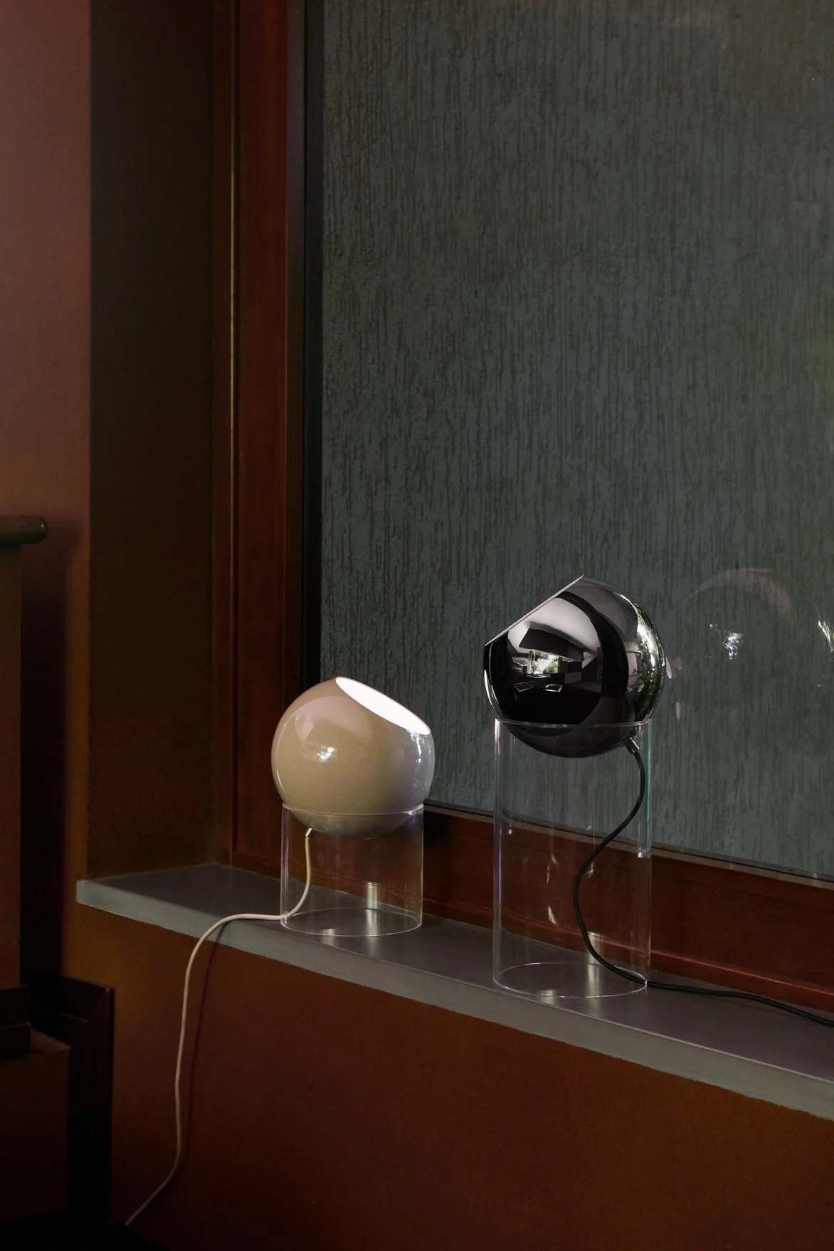 Auf einer Fensterbank stehen zwei Topan-Tischleuchten in verschiedenen Größen von &Tradition in beige und schwarz.