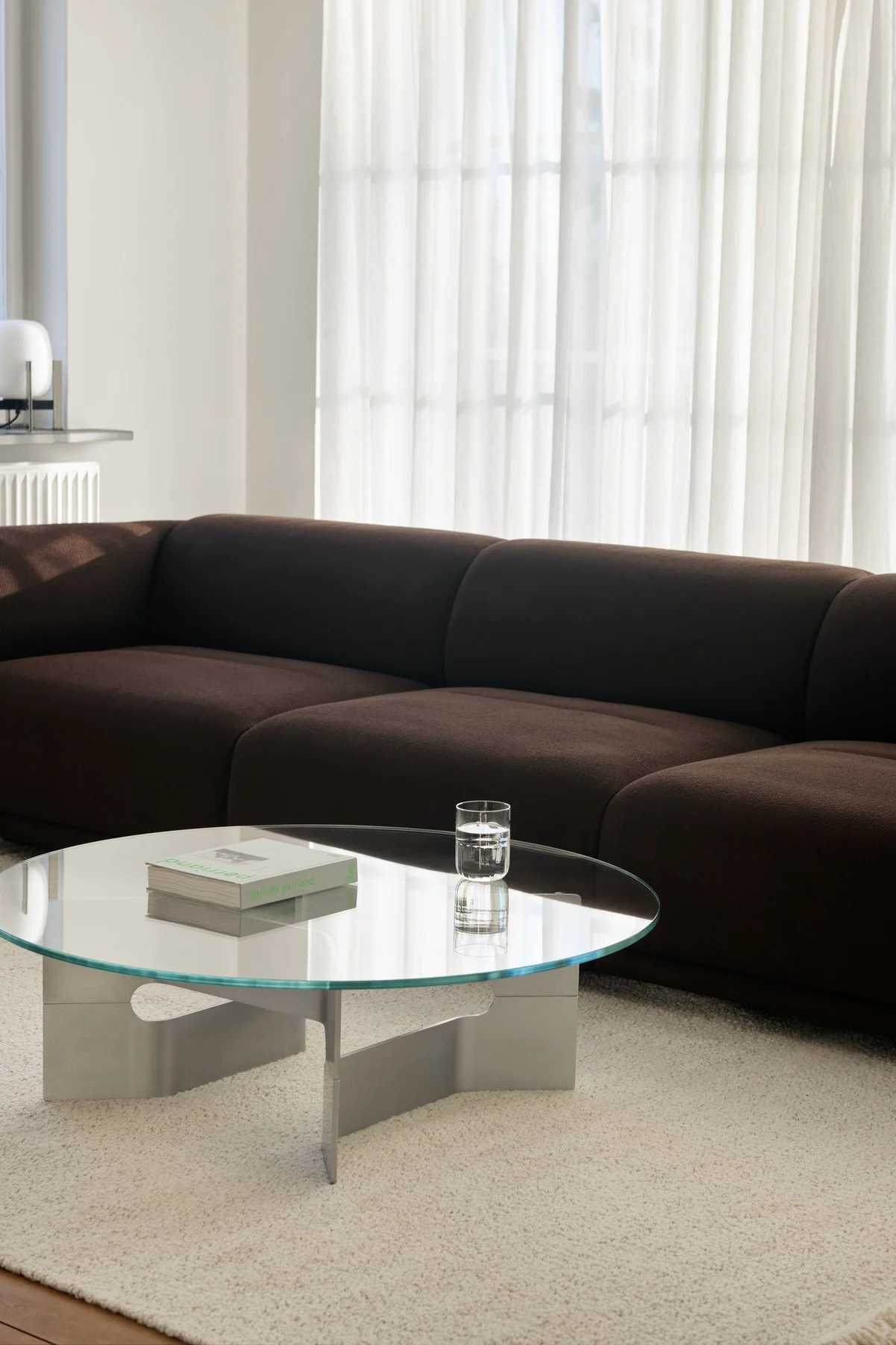 Modernes Wohnzimmer mit dunkelbraunem Modulsofa, rundem Glastisch und hellem Teppich.
