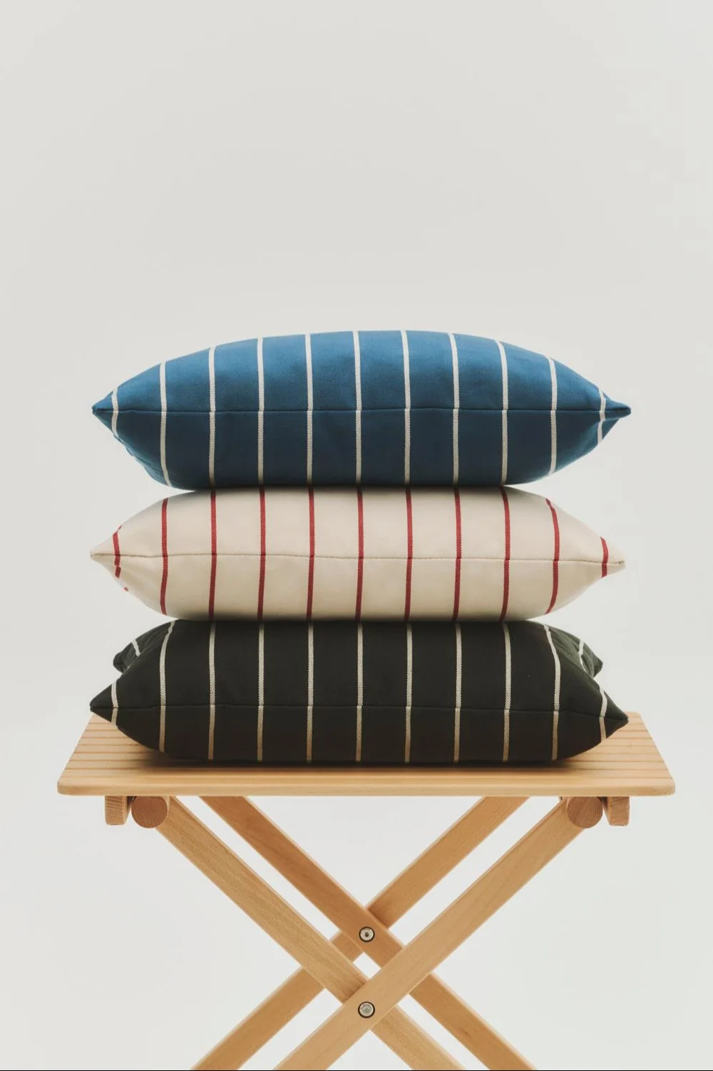 Gestaßelte blaue, cremefarbene und dunkle gestreifte Kissen auf einem klappbaren Holztisch.