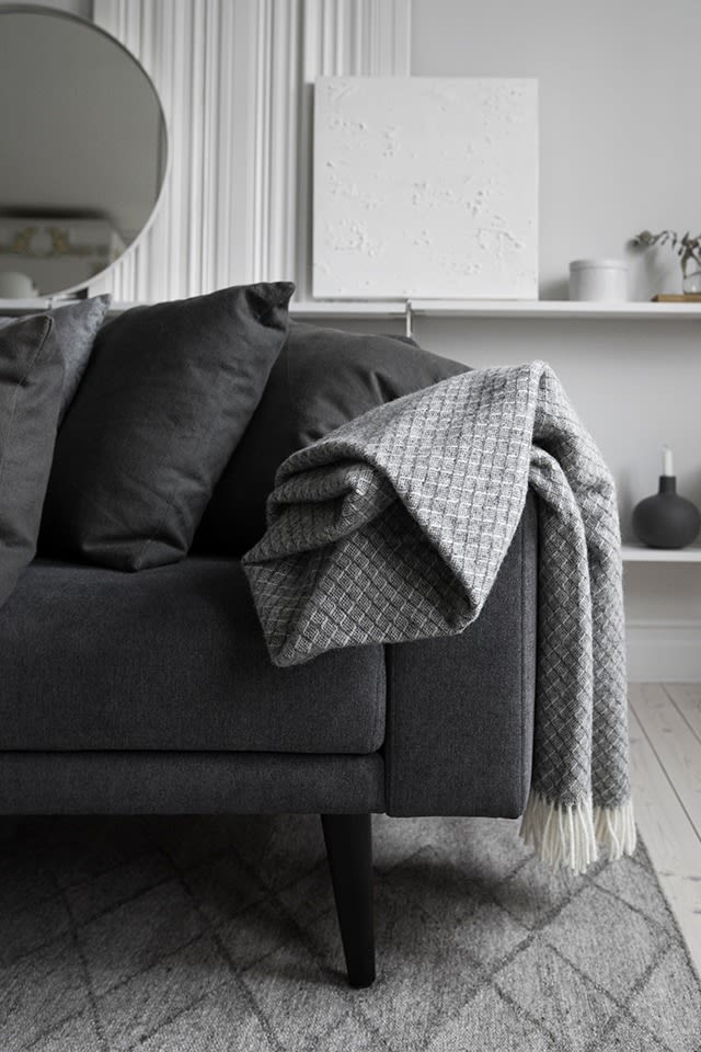 Eine Wolldecke hängt über der Rückenlehne eines Sofas in einem grauen Wohnzimmer.  