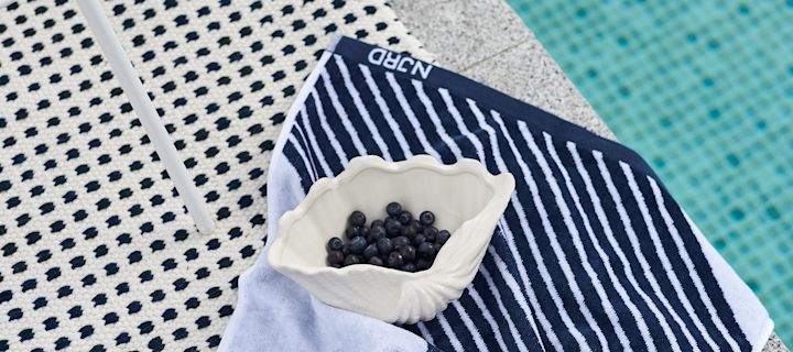 Blaues Stripes Badetuch von NJRD mit Muschelschale von By On mit Blaubeeren am Pool.