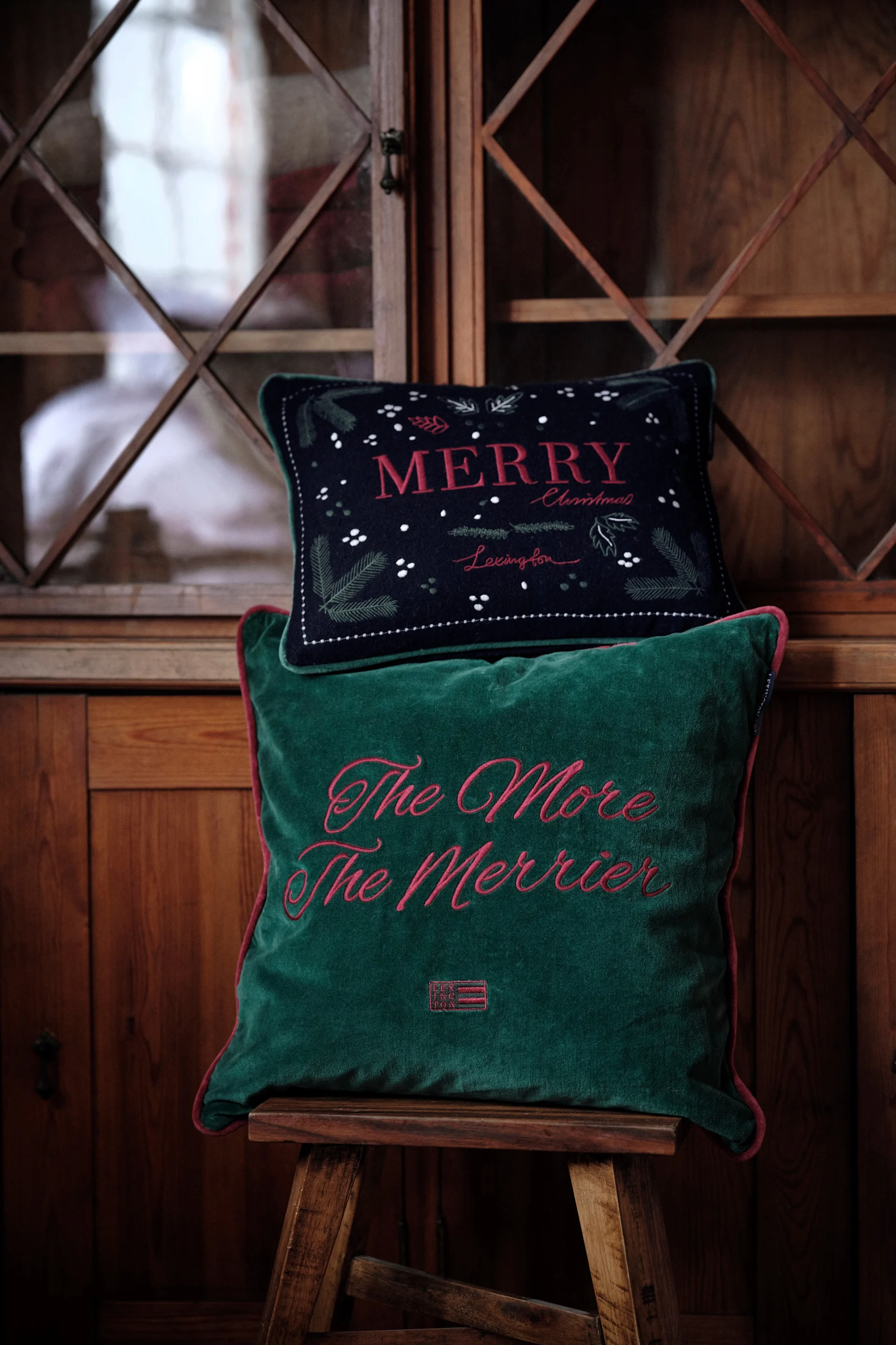 Kissen sind eine beliebte Weihnachtsdeko 2025: Hier stehen zwei weihnachtliche Kissen von Lexington auf einem Hocker.