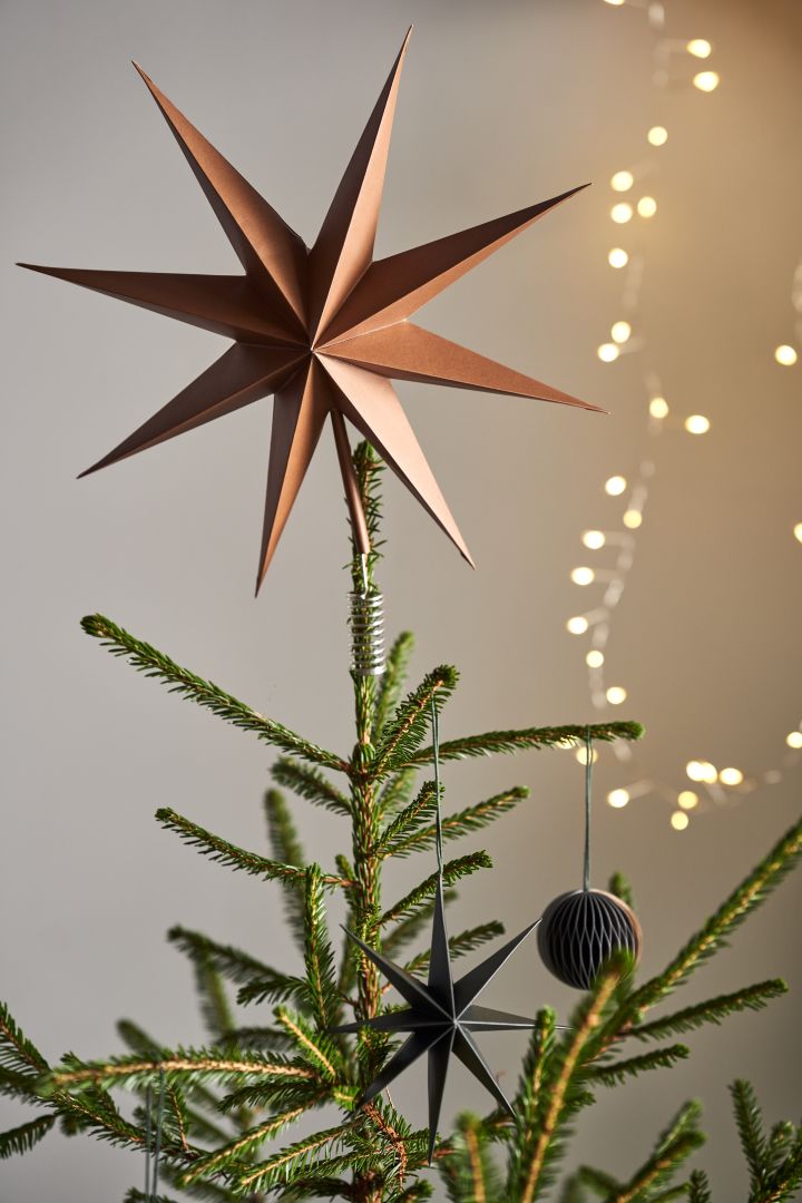 Dekorieren Sie Ihren Baum dieses Jahr mit dem Weihnachtsbaumschmuck 2021 in den 4 verschiedenen Stilen der Nest Trends – Nurture, Share, Boost und Cultivate.  Hier sehen Sie die Sternenspitze von Broste Copenhagen in einer gold-braunen Farbe neben einer zarten Lichterkette. 