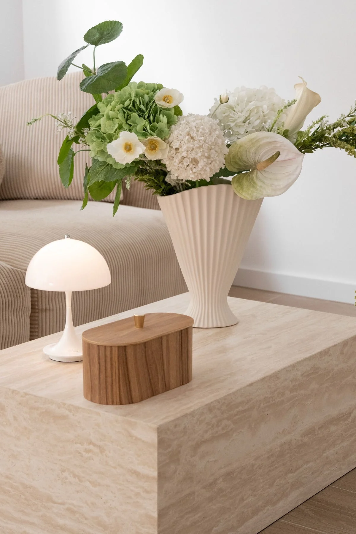 Der beigefarbene Beistelltisch aus Marmor von @by.damira, dekoriert mit der Fountain Vase in Beige von Ferm Living, einer Holzdose und der weißen Panthella Tischlampe von Louis Poulsen.