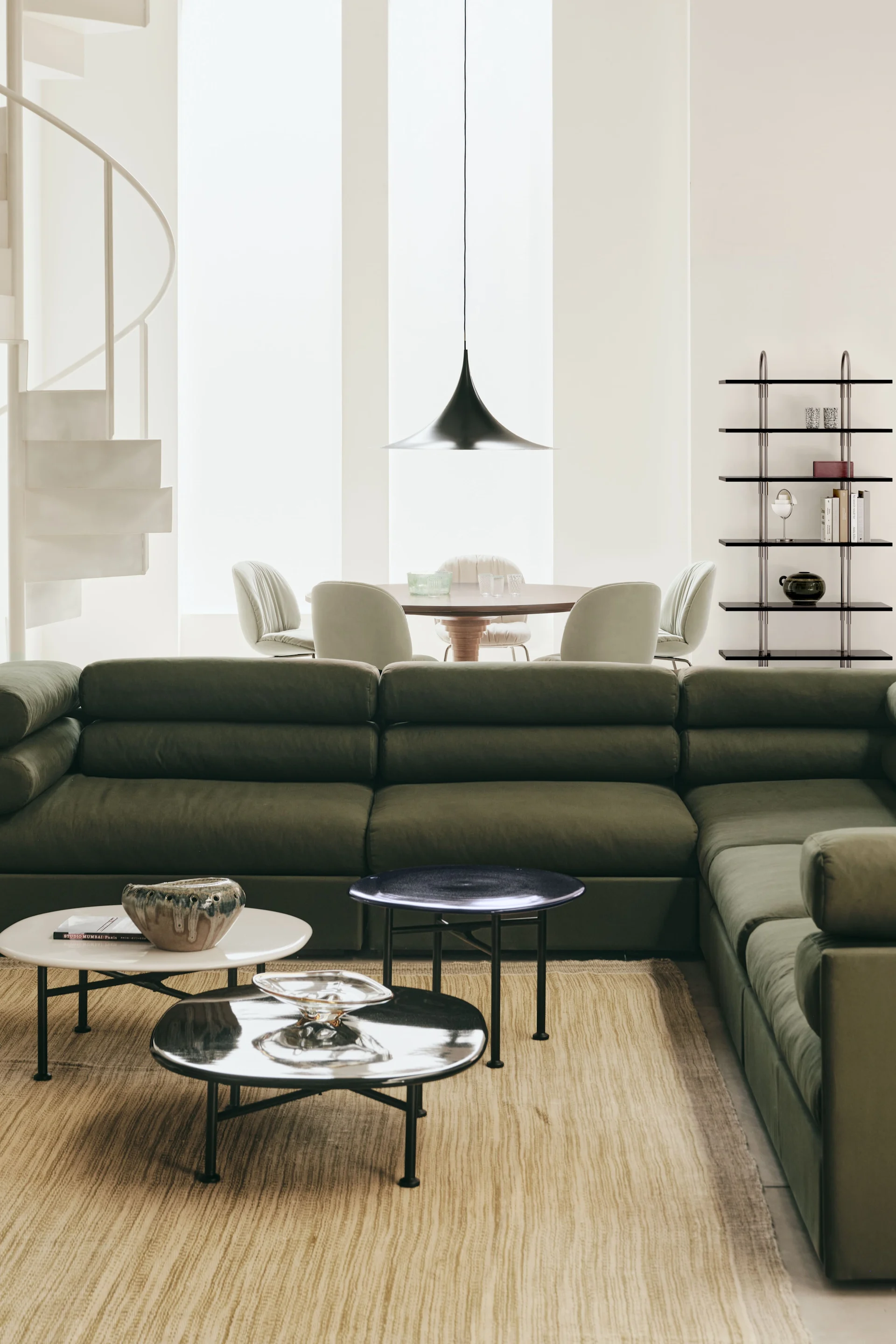 Die passende Deckenleuchte fürs Wohnzimmer: Hier hängt die Semi-Pendelleuchte von Gubi in einem mit grünen Möbeln eingerichteten Wohnzimmer.