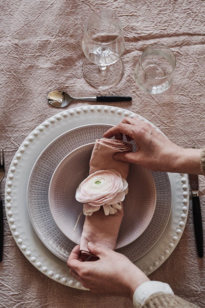 Ein Tipp zum Falten von Servietten ist, die Leinenserviette wie hier gezeigt zu rollen und mit einer Blume als Dekoration auf den Teller zu legen. 