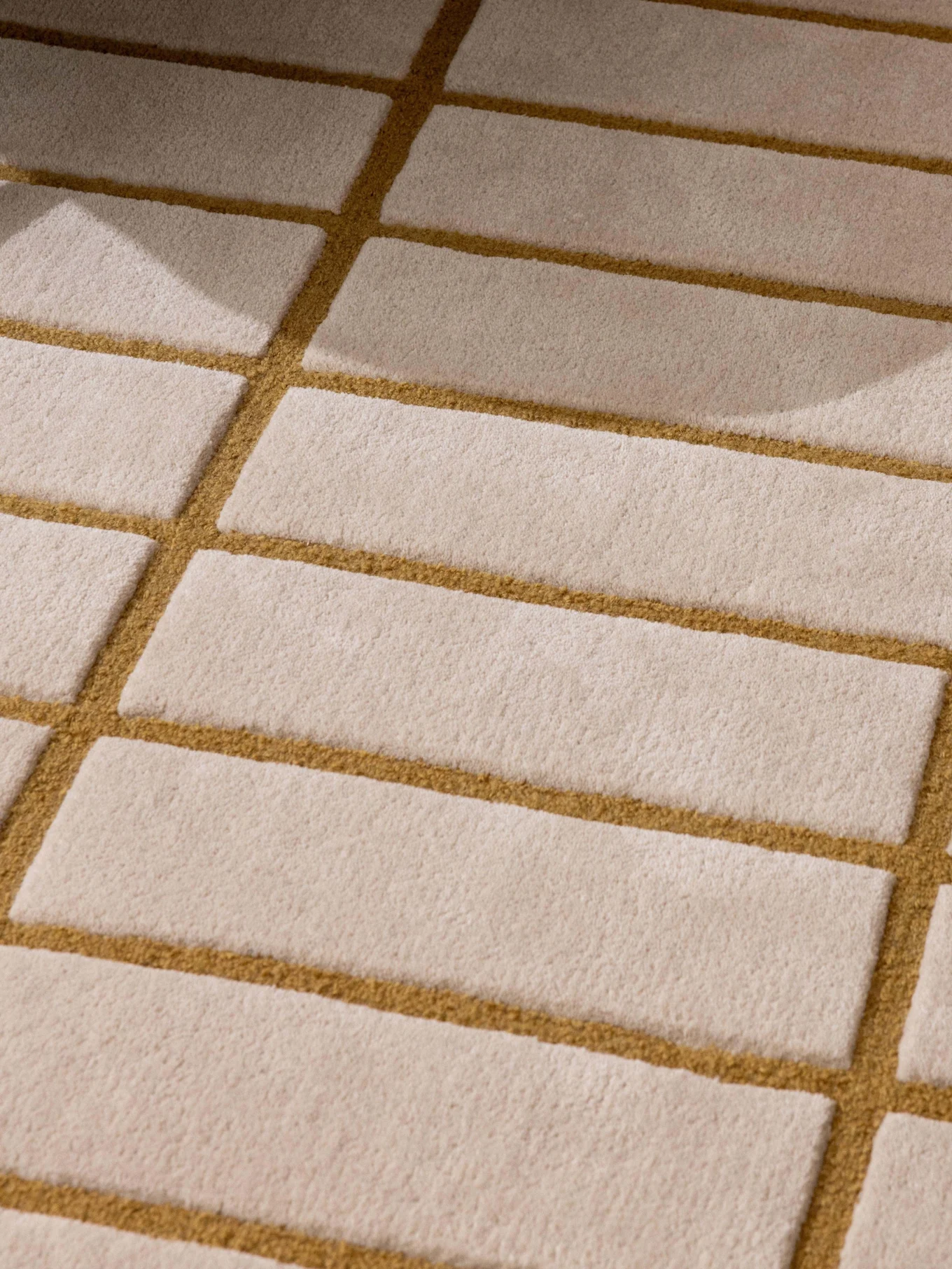 Gemusterter beige-goldbrauner Teppich, grünes Sesselbein und ein Tablett mit weißer Teekanne und Tasse.