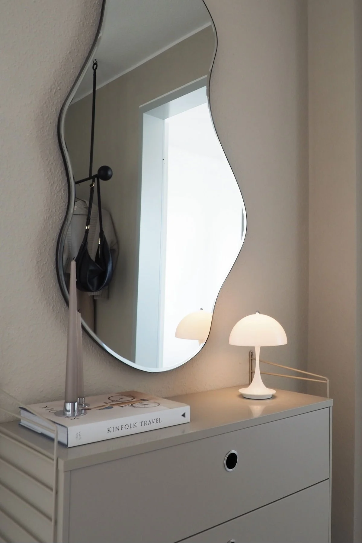 Die passende Beleuchtung ist wichtig für die Gestaltung eines Flurs. Hier sehen Sie die weiße kabellose Panthella Tischlampe von Louis Poulsen auf einem String Schränkchen, darüber hängt der Pond Spiegel von Ferm Living.