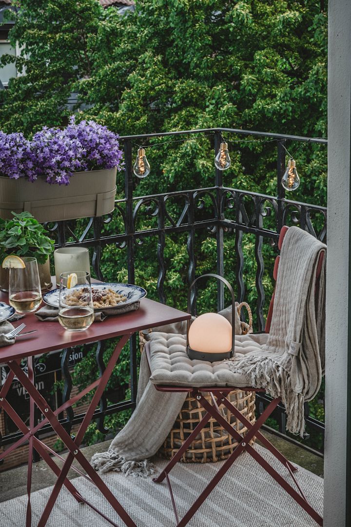 Dekorieren Sie einen kleinen Balkon mit Lichterketten und tragbaren Leuchten, wie dieser Carrie-Lampe von Menu, für eine gemütliche Atmosphäre bei Einbruch der Dunkelheit. 