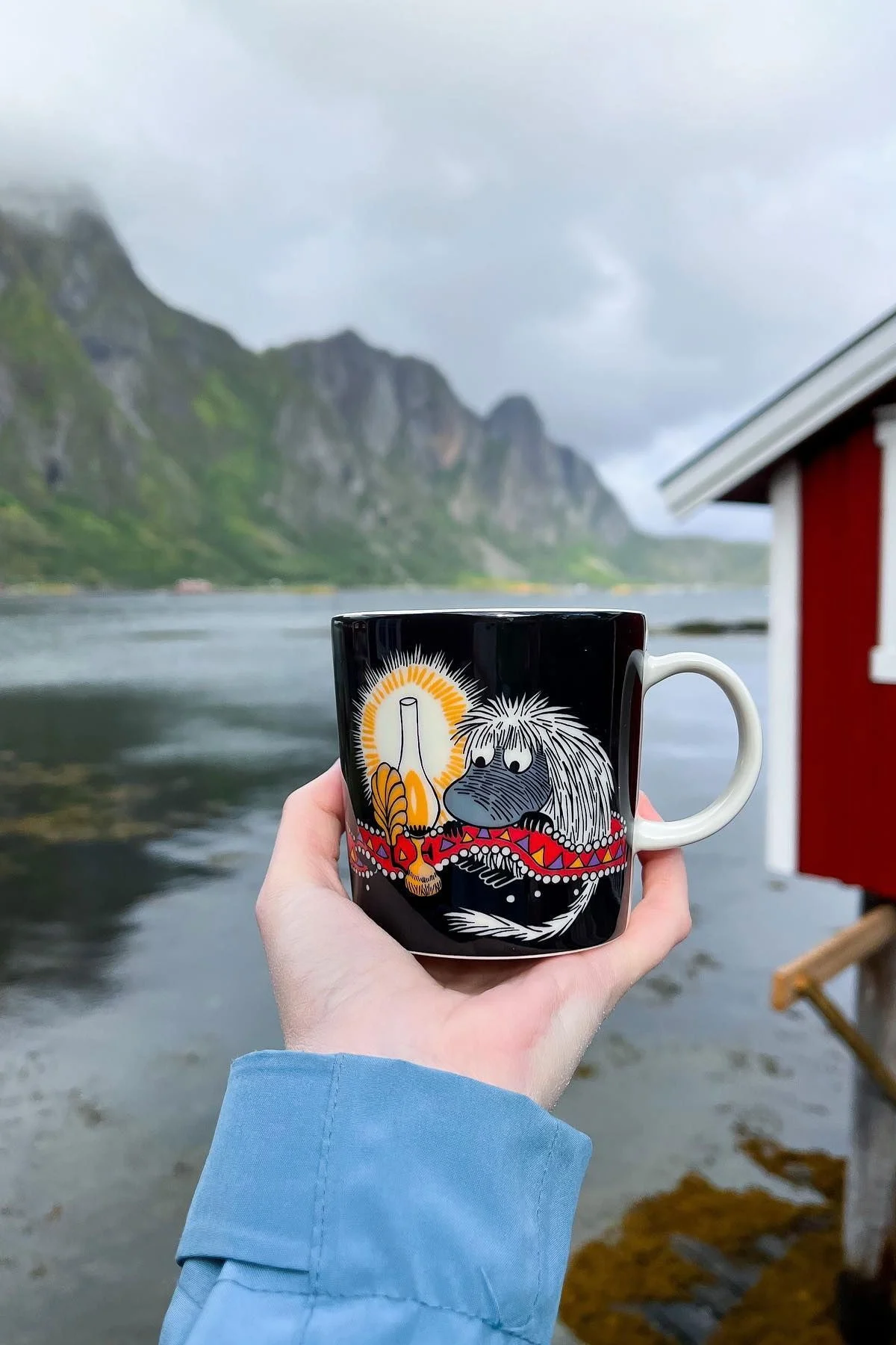 @moominbyingri hält die Urahn-Mumintasse in der Hand, im Hintergrund eine raue norwegische Landschaft.