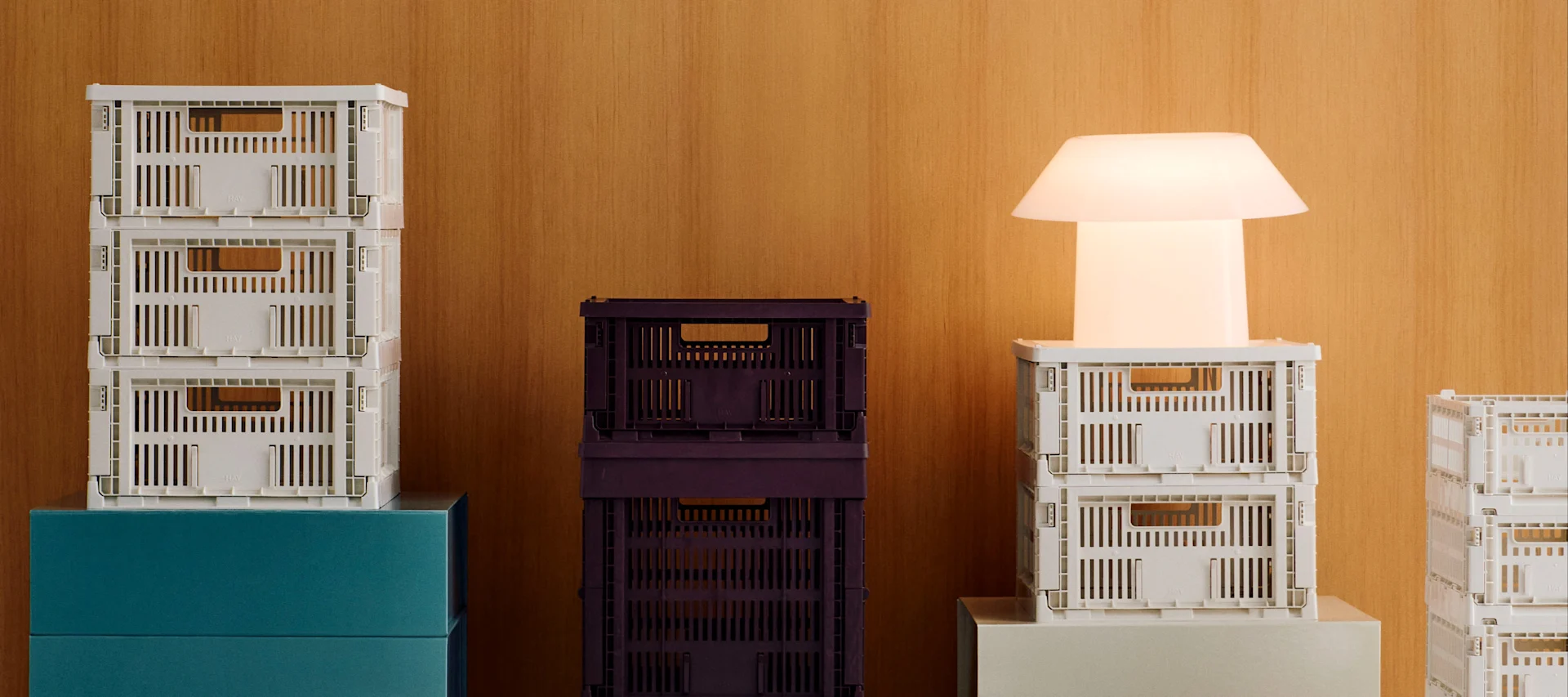 Stapel von weißen und dunkelvioletten faltbaren Kisten mit einer leuchtenden weißen modernen Lampe vor einem Holzhintergrund.