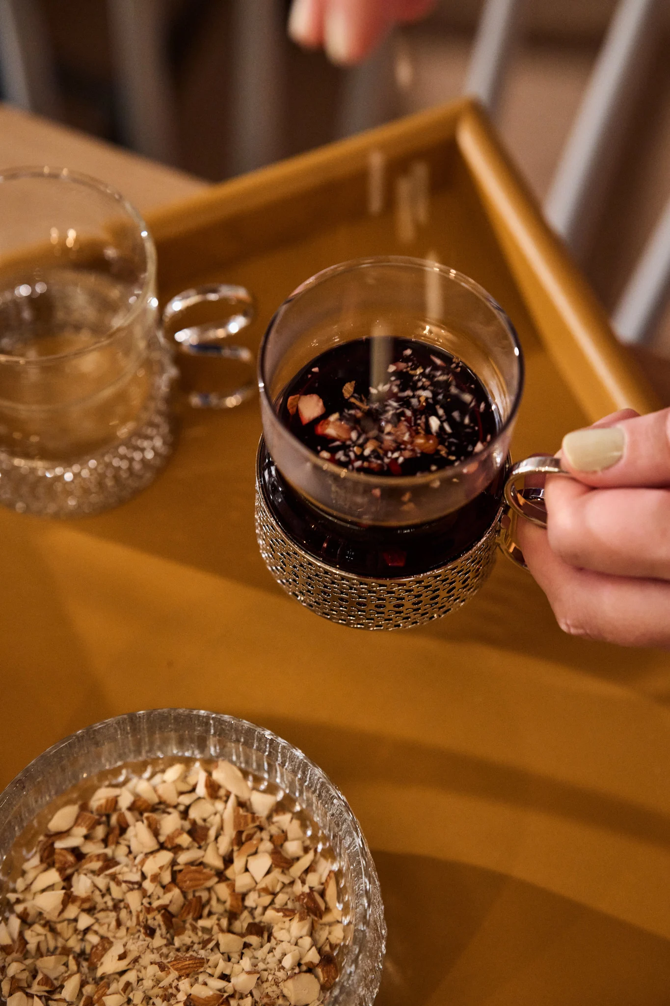 Schwedischer Glühwein, Glögg, gehört zu Weihnachten in Schweden dazu. Hier hält eine Hand eine Tasse mit Glögg und lässt gehackte Mandeln hineinrieseln.
