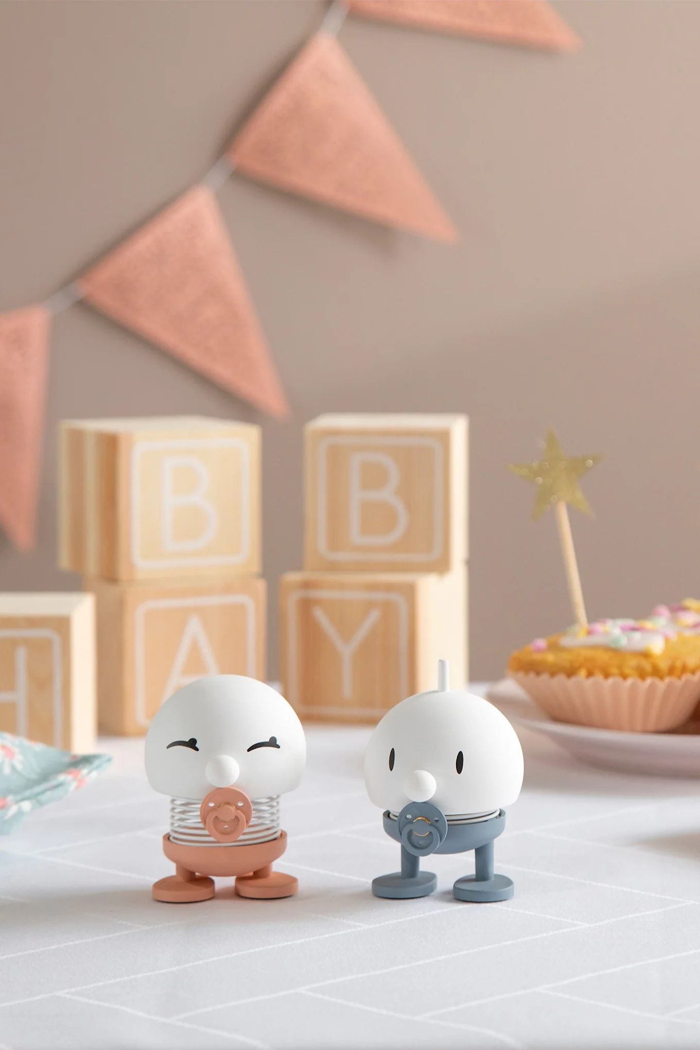 Die Hoptimisten Baby Bimble sind in Rosa und Blau erhältlich und stehen auf einem mit Geschenken, Girlanden und Muffins dekorierten Tisch.