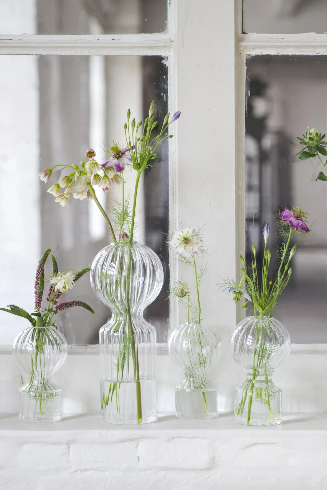 Auf einer Fensterbank stehen die drei Mini-Vasen Iki Doll von Serax mit einzelnen Stängeln darin.