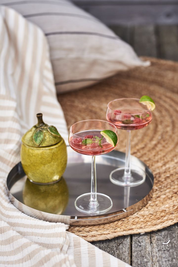 Iittala Essence Cocktailglas mit Sommergetränk in auf einer Silberplatte auf Jutematte am Meer.