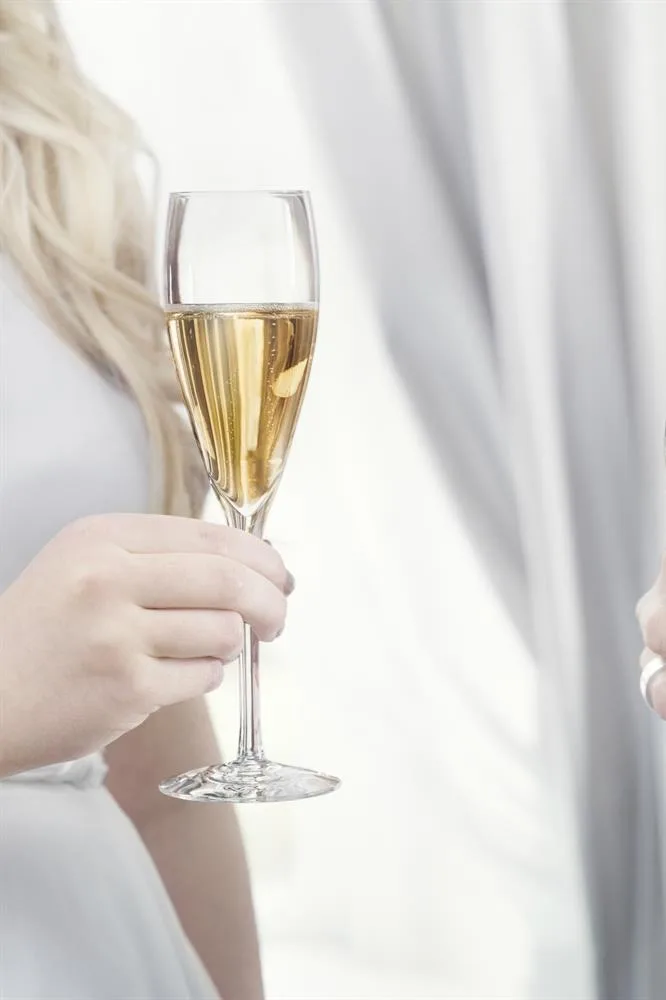Eine Frauenhand hält ein gefülltes More Champagnerglas von Orrefors - eine klassische Hochzeitsgeschenk-Idee.
