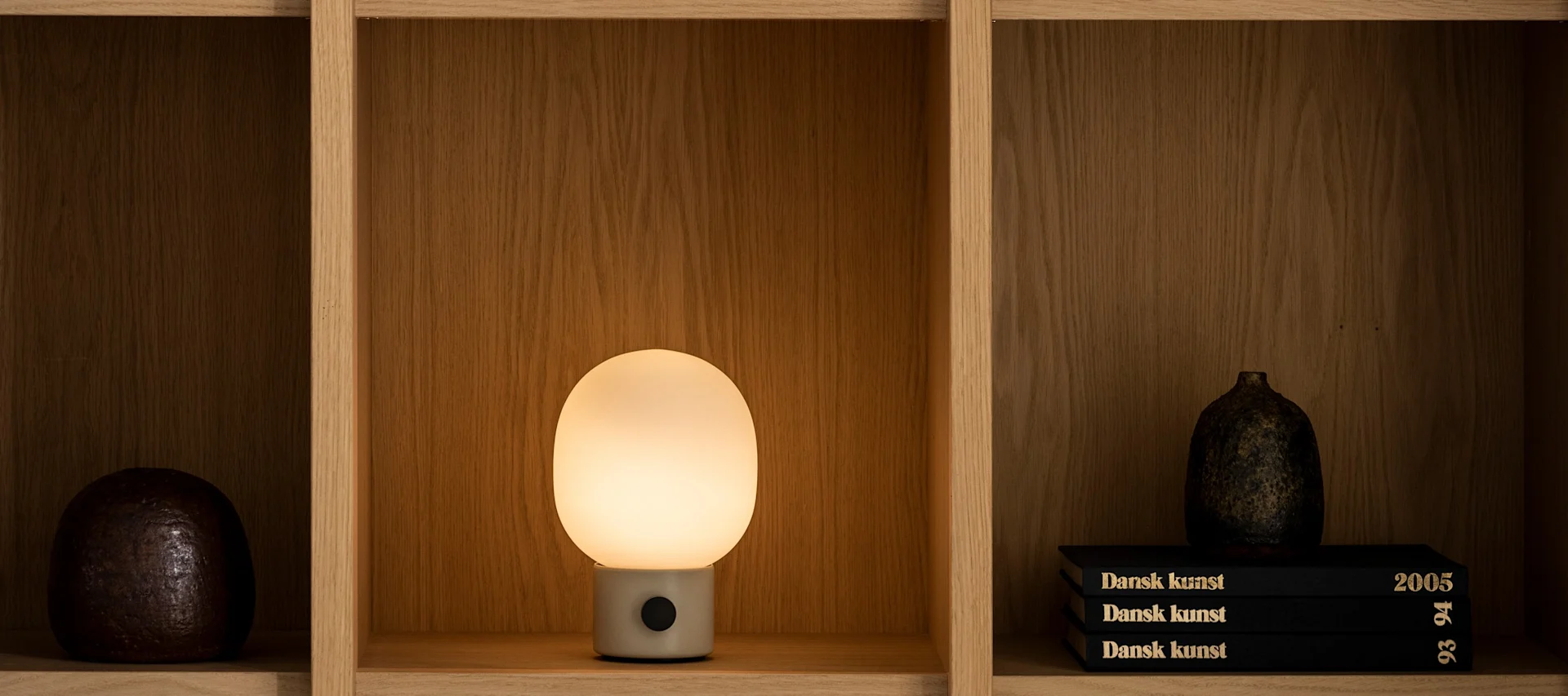 In einem Regal steht eine leuchtende JWDA-Tischlampe von Audo Copenhagen.