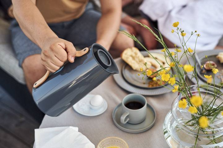 An Sommermorgen werden Frühstück und frisch gebrühter Kaffee genossen, der aus grauen Stelton-Thermoskannen ausgeschenkt wird. 