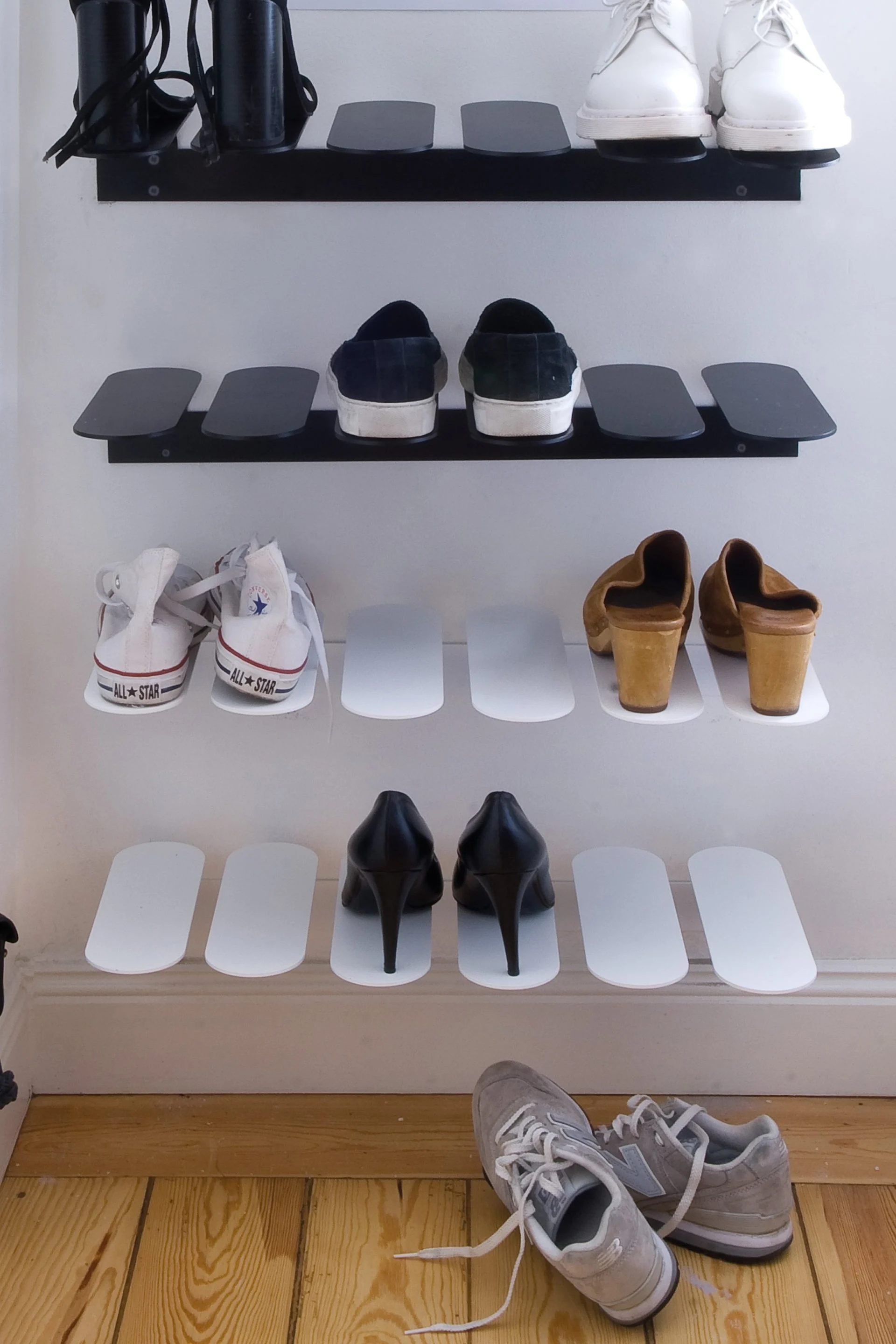Verschiedene Schuhe auf wandmontierten Regalen, darunter schwarze Absätze, weiße Sneaker, dunkle Slip-Ons, Clogs und graue Sneaker.