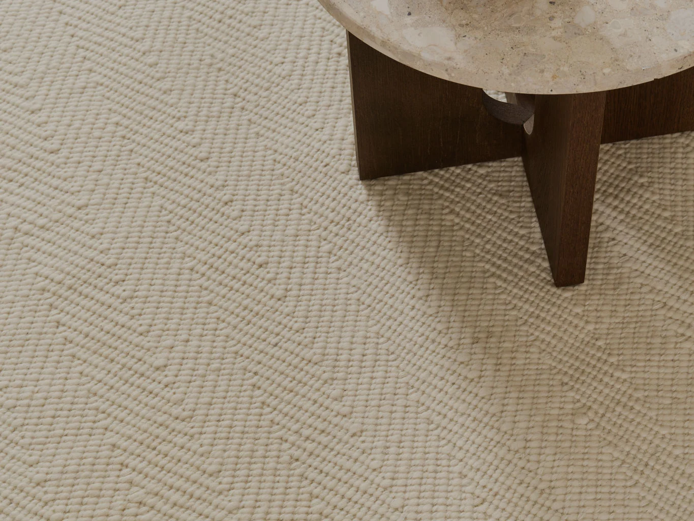 Nahaufnahme eines cremefarbenen strukturierten Teppichs mit Chevron-Muster, neben einem Tisch mit Steinplatte.