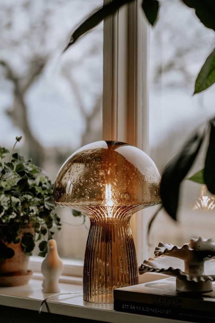 Die braune Fungo Tischlampe von Globen Lighting steht, umgeben von Pflanzen, auf einer Fensterbank - die perfekte Boho Deko.