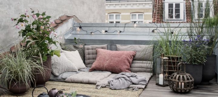 Tipps für einen Balkon im Boho Style – hier eine gemütliche Kuschelecke mit vielen Kissen, Decken und Pflanzen.