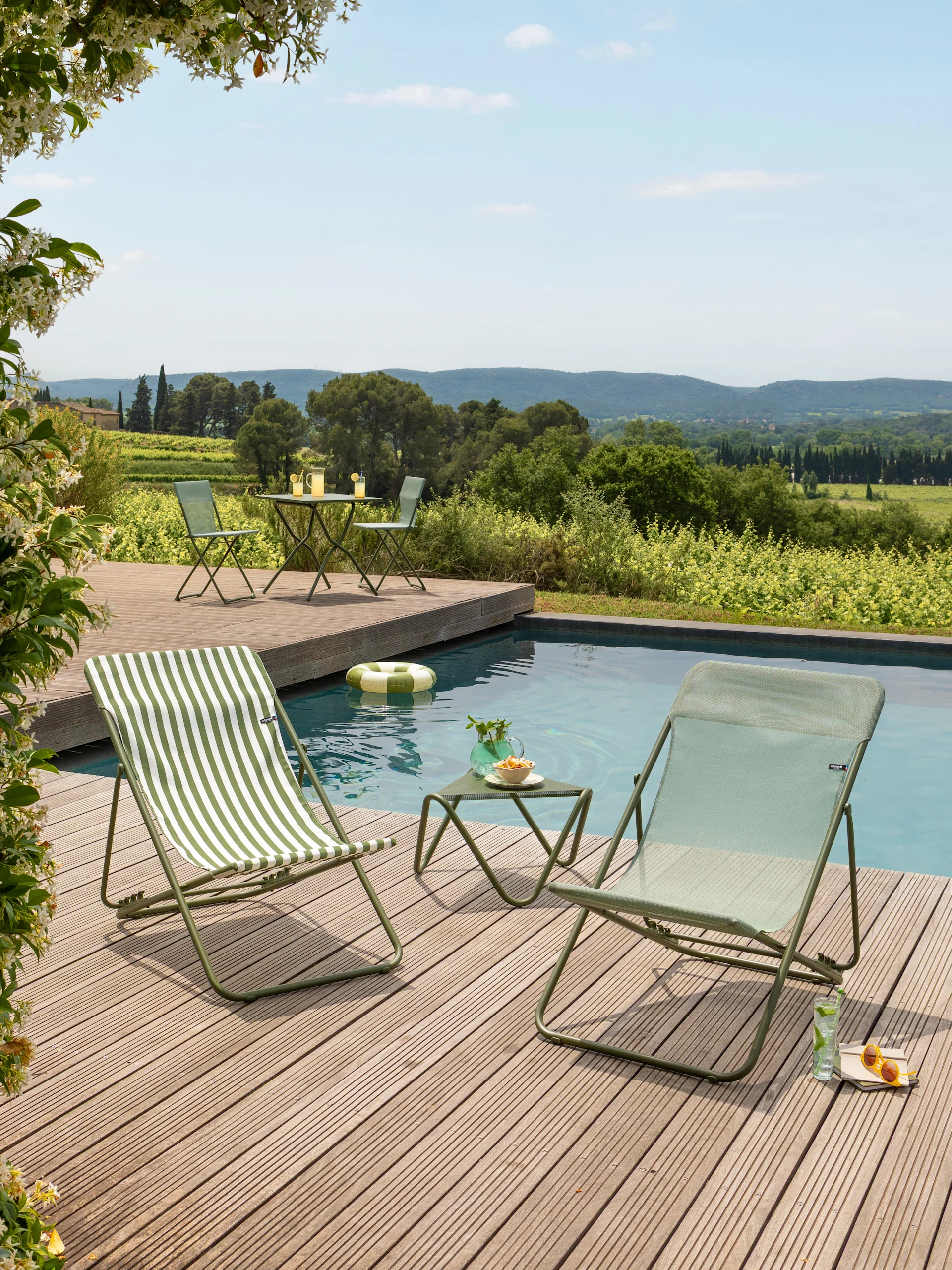 Zwei grüne Outdoor-Liegen, eine gestreift, und ein Tisch am Pool, mit Blick auf Weinberge.