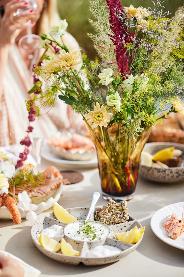 Ein zum Krebsfest in Schweden gedeckter Tisch mit einem Blumenstrauß in der gelben Viva Vase und dem Ditte Servierteller, beides von Sagaform.