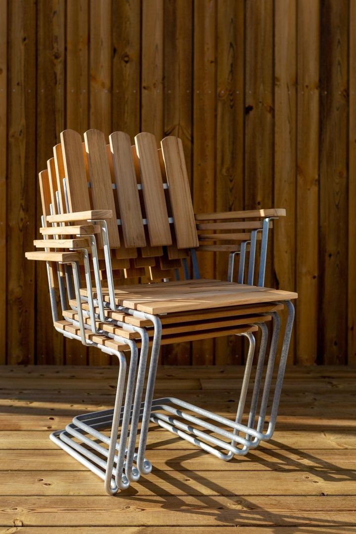 Grythyttan Reportage: Hier sehen Sie gestapelte A2-Stühle mit Armlehnen aus Holz auf einer Terrasse stehen.