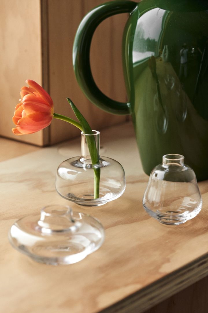 Frühlingserwachen: Hier sehen Sie drei Mini-Vasen von Kosta Boda auf einer Fensterbank stehen, eine davon mit einer frischen roten Blume darin.