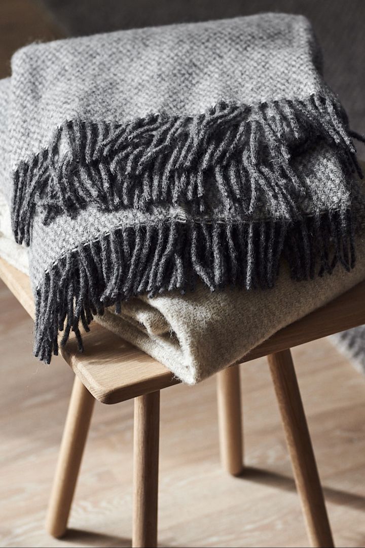 Eine Kuscheldecke ist eine klassische Hochzeitsgeschenk-Idee. Hier liegt die graue Sandstone Decke von Scandi Living auf einem Hocker.