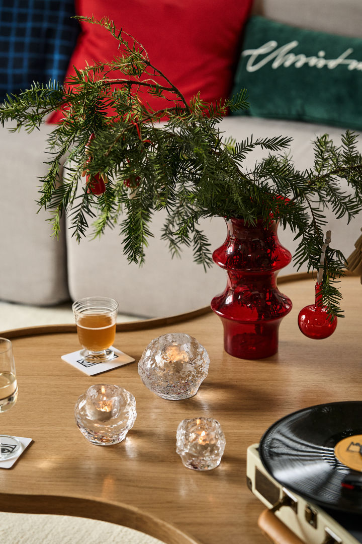 Geschenlideen zu Weihnachten: Hier sehen Sie einen Holztisch mit einer Vase und Tannengrün darin, davor stehen drei Windlicher der Snowball-Kollektion von Kosta Boda.