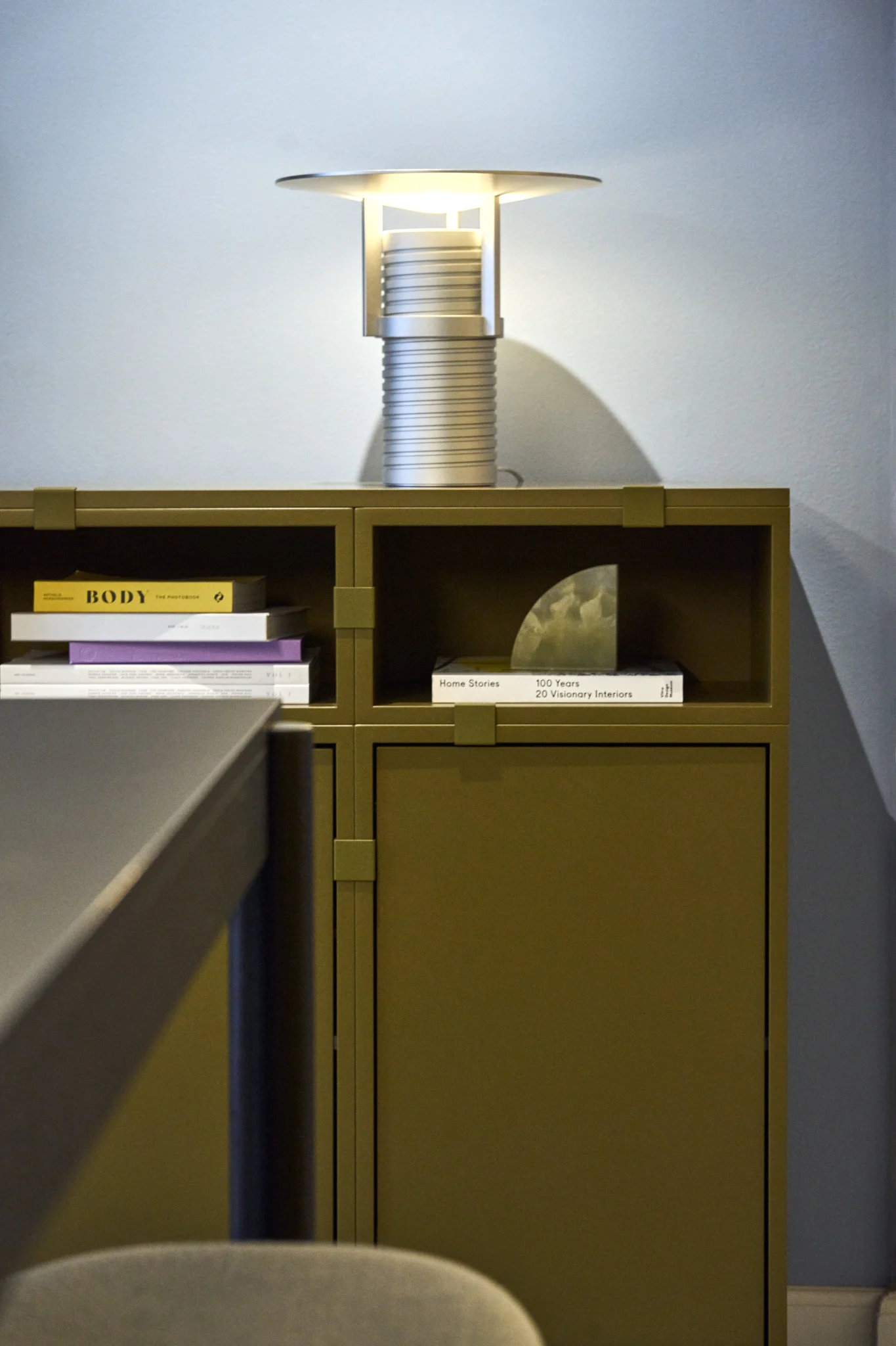 Ein grünes Regal, gebaut aus der Stacked-Kollektion, darauf die silberne Set Tischleuchte, alles von Muuto.