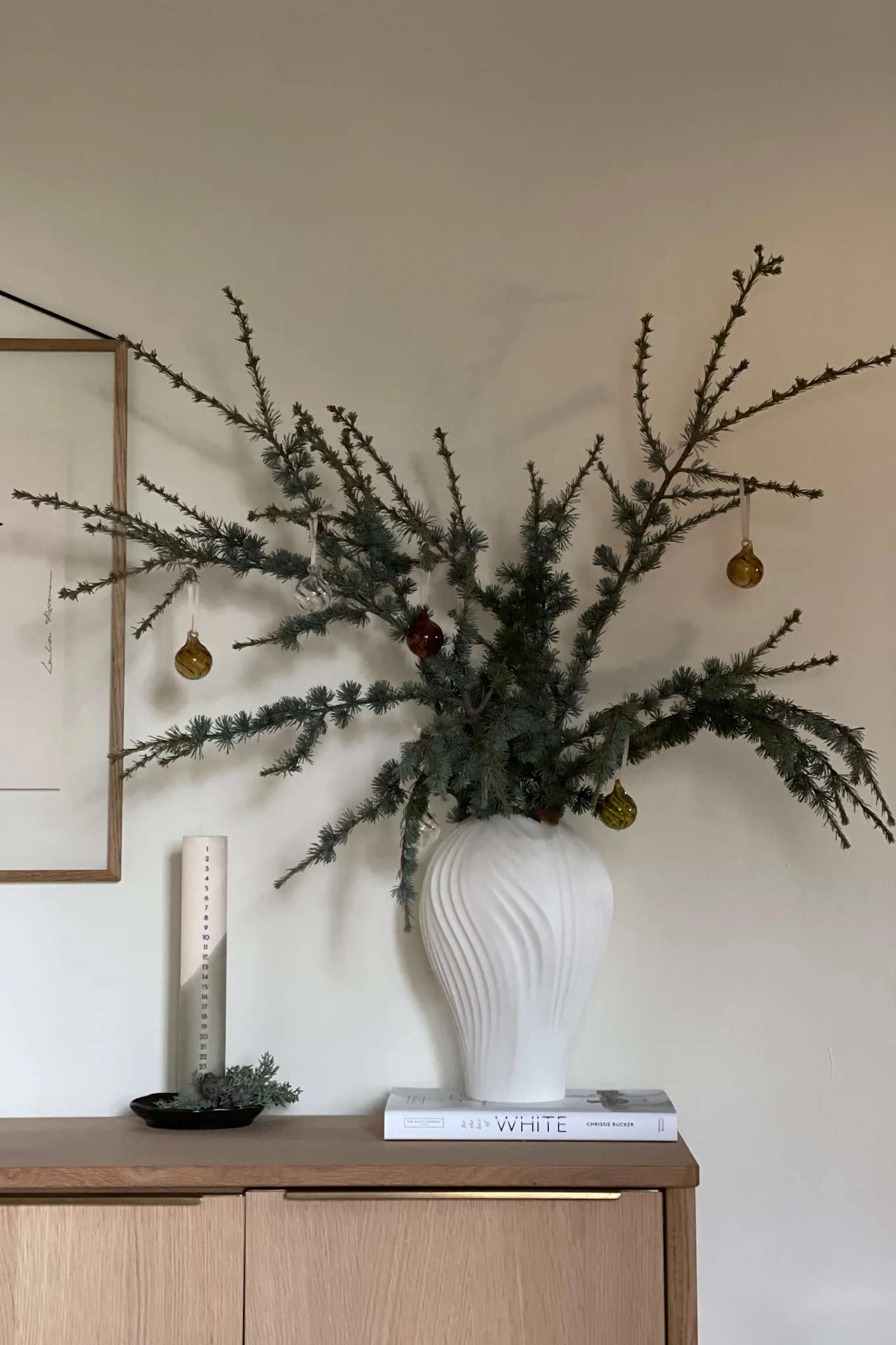 Moderne Weihnachtsdekoration verwendet natürliche Materialien, Tannenzapfen und Zweige sowie eine neutrale Farbpalette, wie diese Zweige in einer Vase neben einer Adventskerze.