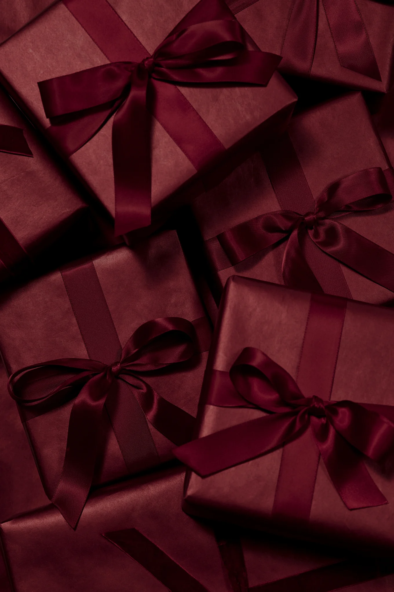 Mehrere dunkelrote Geschenkboxen, verpackt mit passenden Satinbändern und Schleifen.