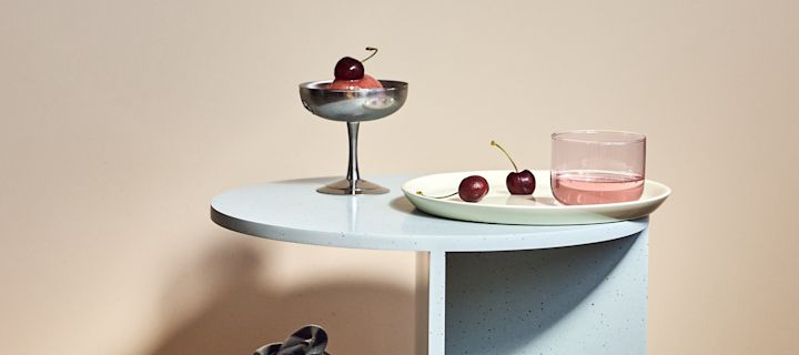 Die Wohntrends 2022 umfassen sanfte Pastellfarben, inspiriert von den 80er Jahren, hier ruht das Tint Trinkglas und die Italian Ice Cup Dessertschale, beide von HAY, auf dem Teema-Teller von Iittala, begleitet von Eis und Kirschen.