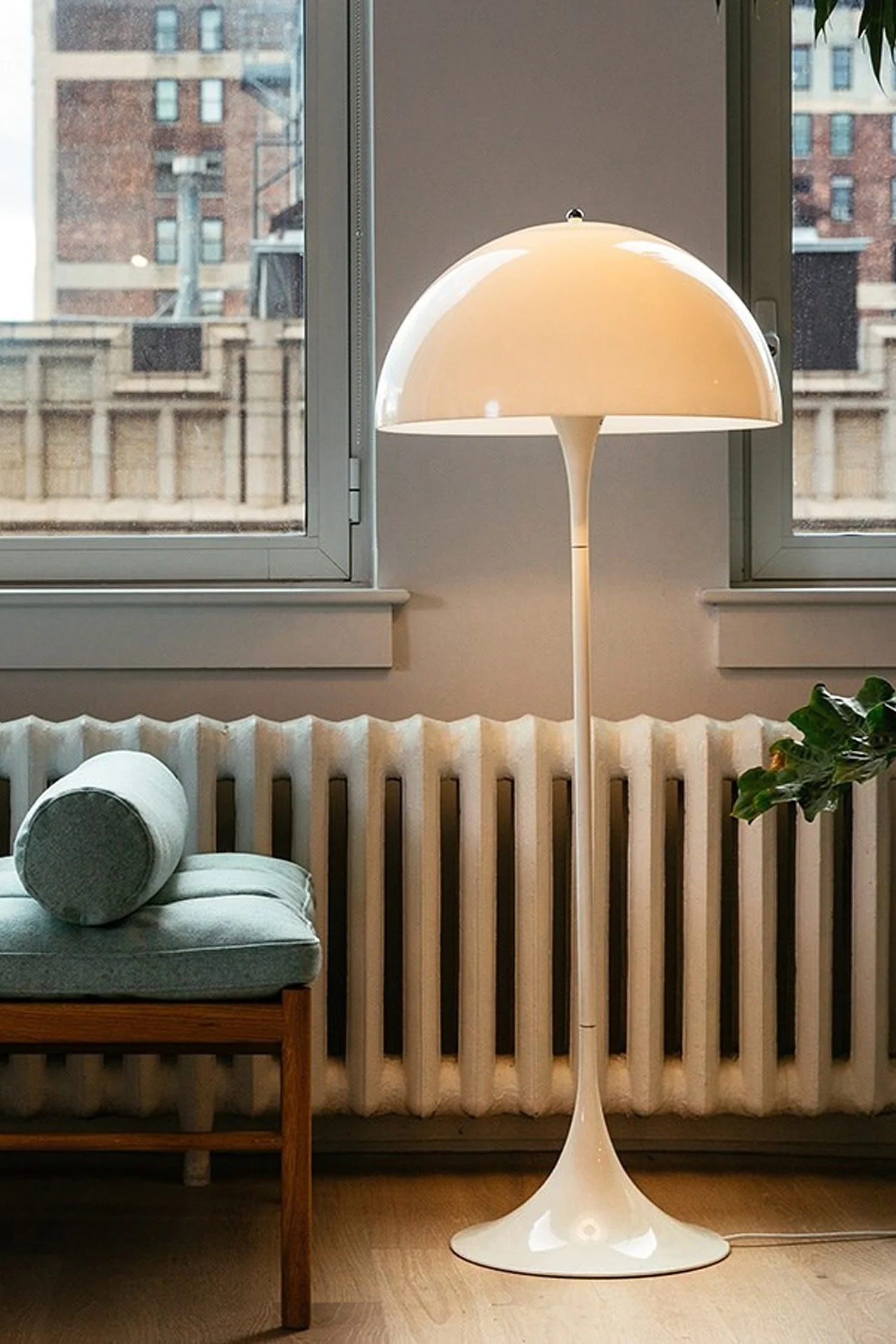 Lichtplanung: Die weiße Panthella Stehlampe von Louis Poulsen gibt ein angenehmes Licht ab und steht hier in einem Wohnzimmer vor einer Fensterfront.