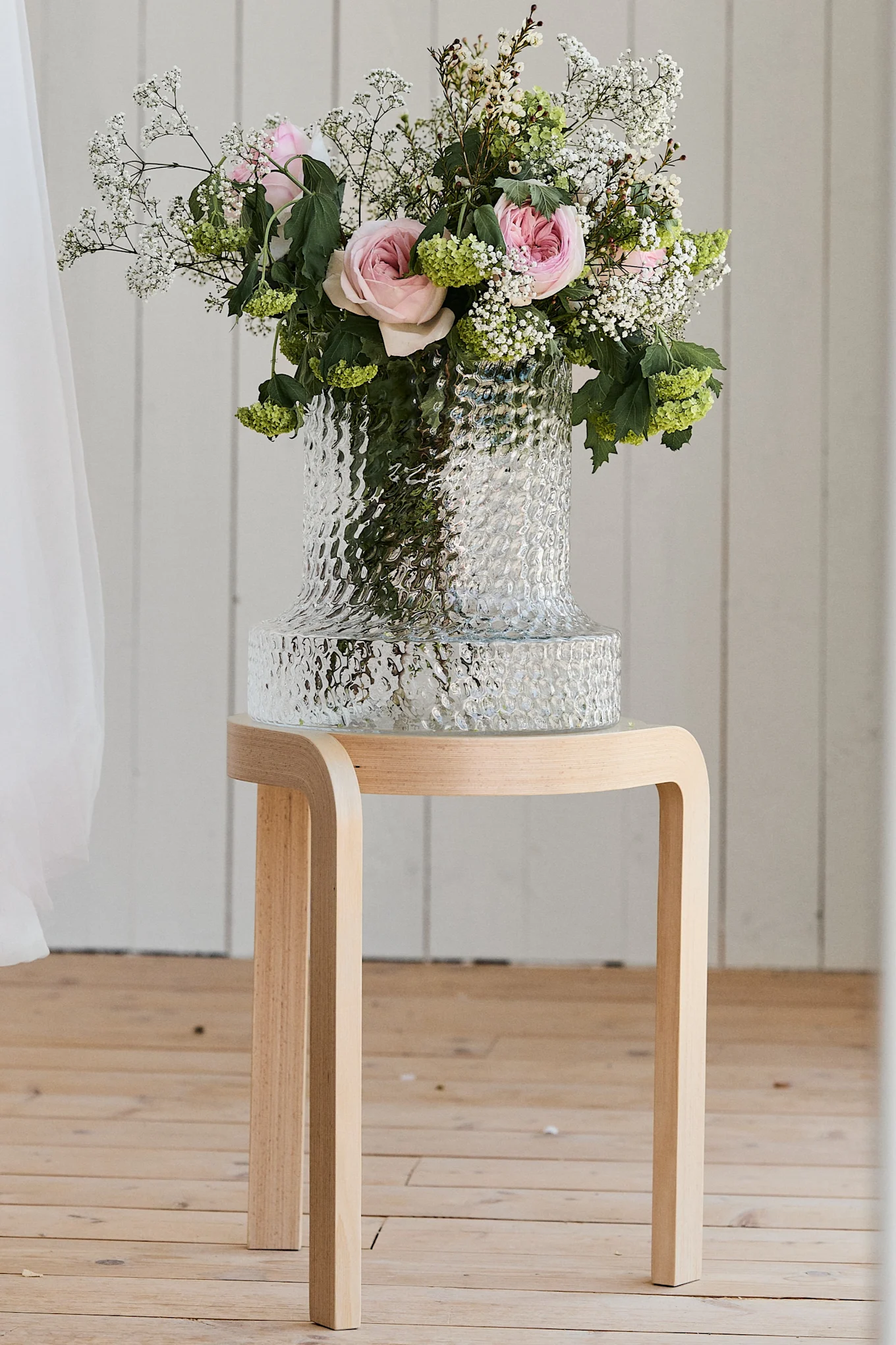 Hochzeitsgeschenk-Ideen: Die Kolonn Vase von Skrufs steht mit einem Brautstrauß auf einem Hocker.