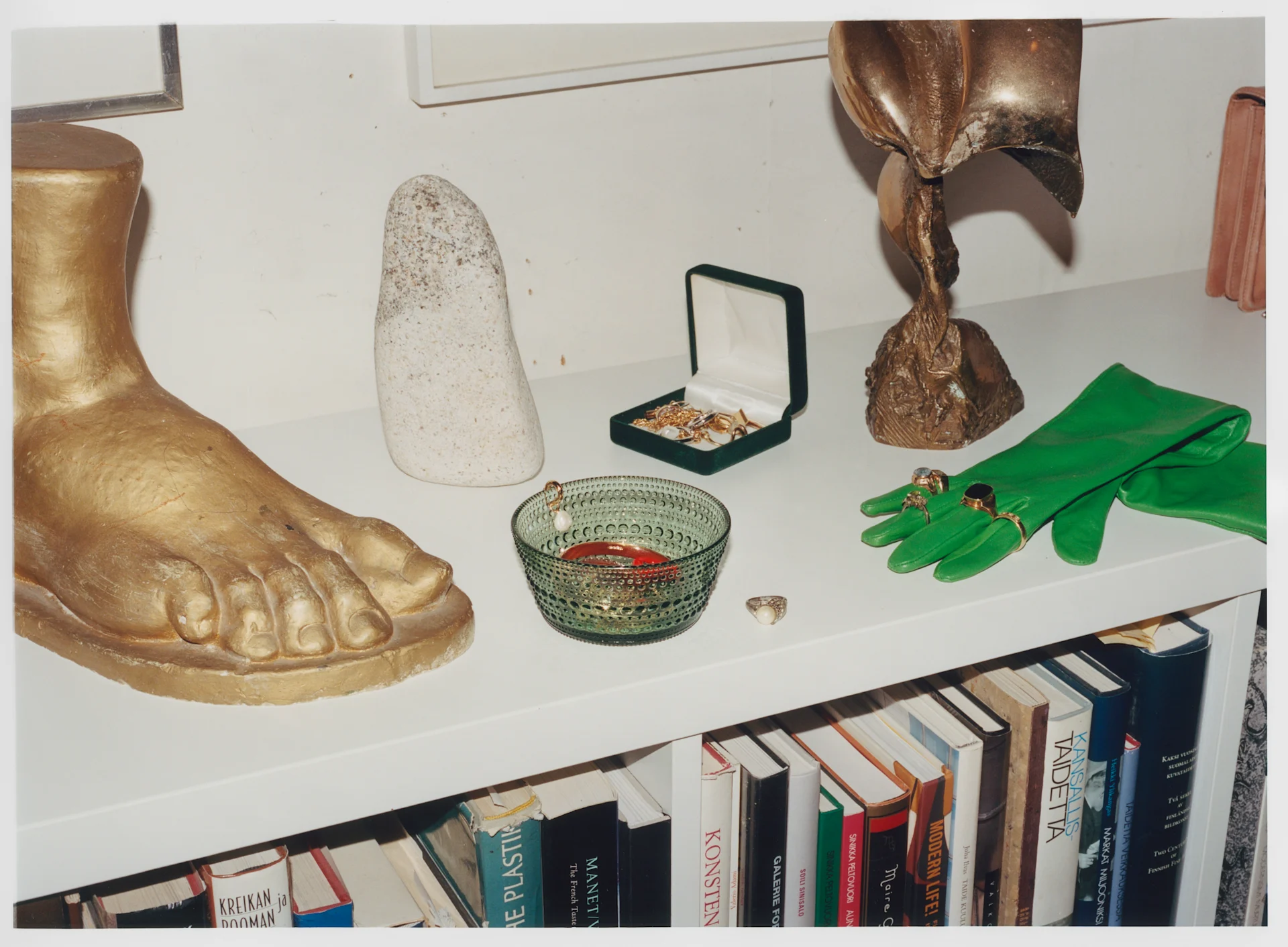 Iittala tritt in eine neue Ära ein, aber die Produkte bleiben dieselben, hier die Kastehelmi-Schale in Grün auf einem Sideboard mit Statuen und Handschuhen.