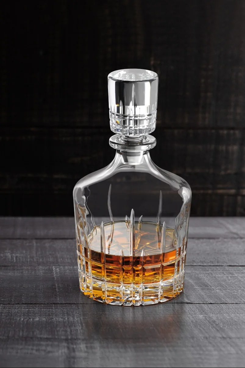 Kristall-Whiskykaraffe gefüllt mit bernsteinfarbener Flüssigkeit auf einem dunklen Holztisch.