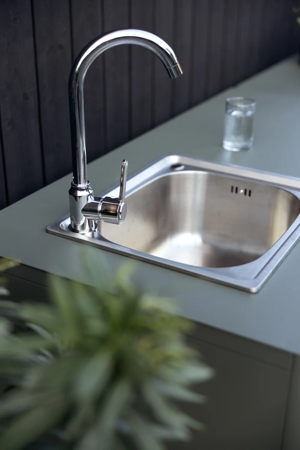 Outdoor-Küchenspüle mit Chromarmatur und einem Glas Wasser auf einer grünen Arbeitsplatte.