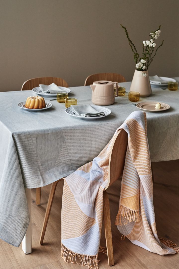 Ein gedeckter Kaffee-Tisch mit Porzellan aus der Lines-Serie und einer rosa-gemusterten Decke über dem Stuhl.