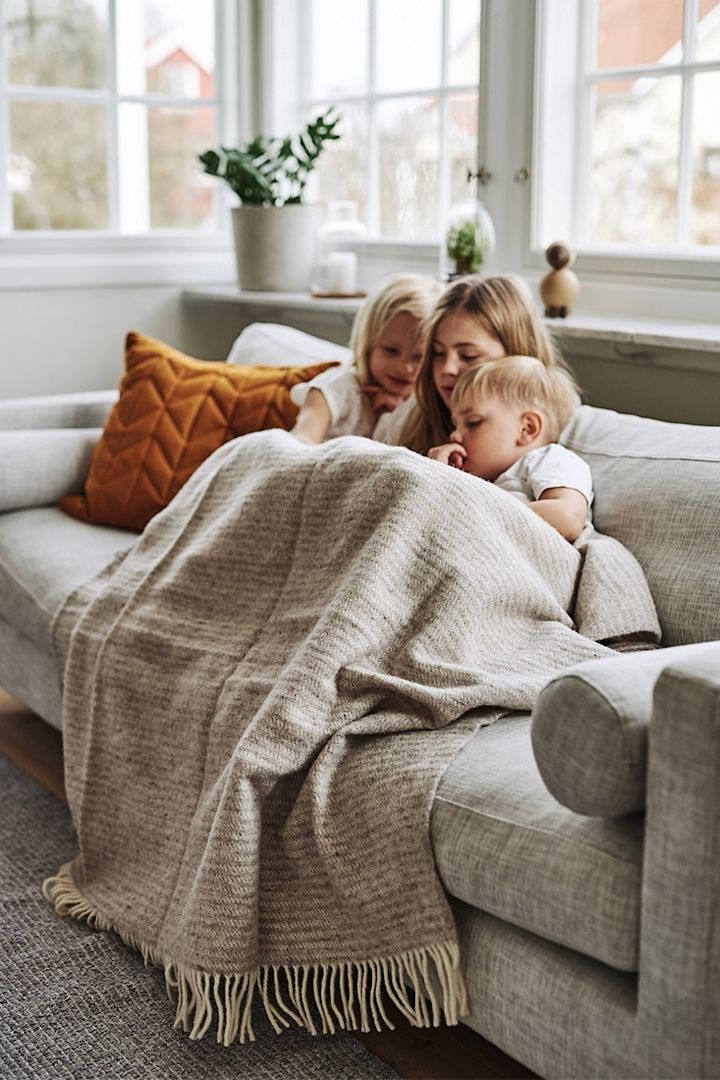 Die Kinder kuscheln sich auf dem Sofa unter eine warme Wolldecke von Klippan Yllefabrik. 