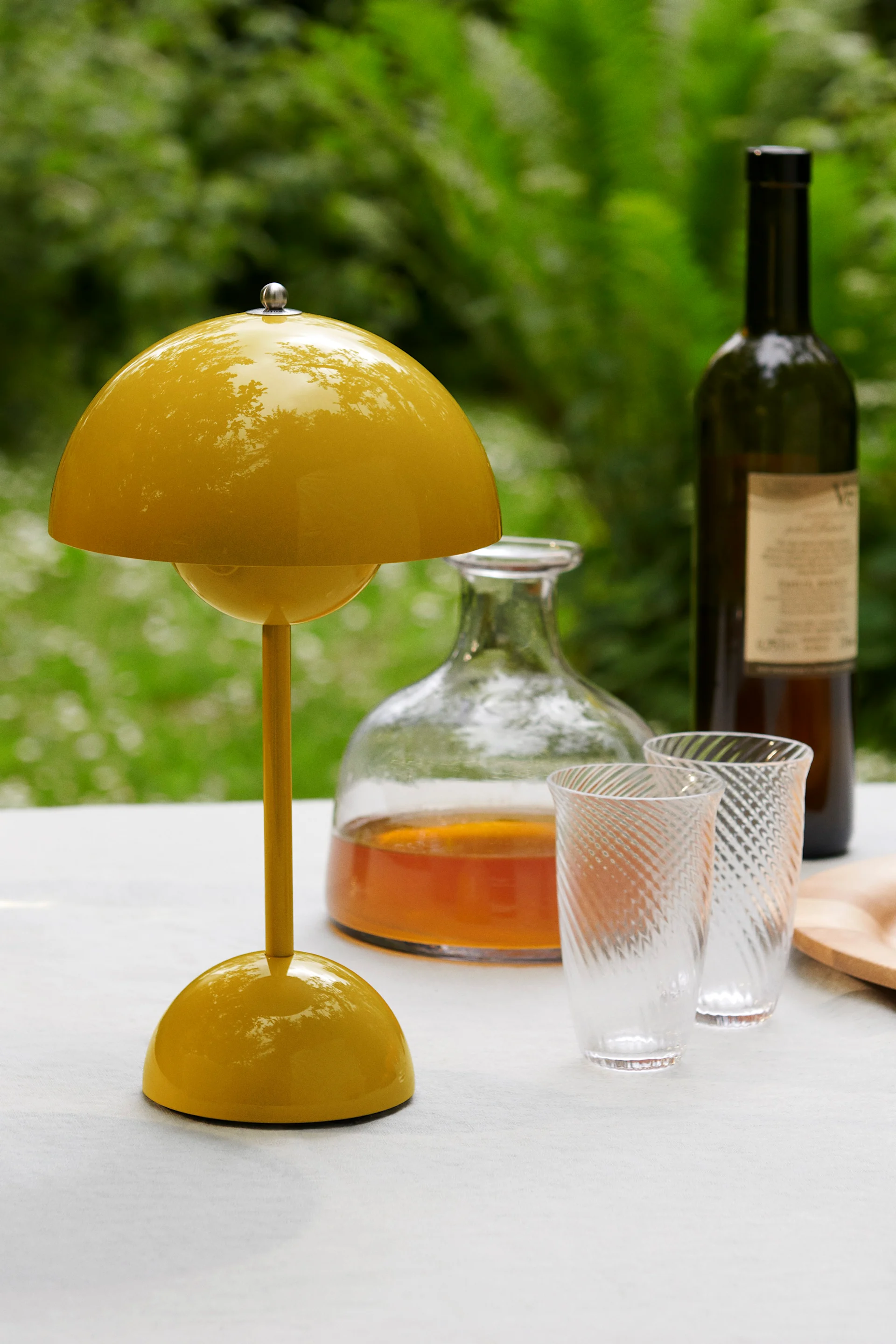 Eine gelbe pilzförmige Tischlampe auf einer weißen Tischdecke im Freien mit Getränken und Snacks.