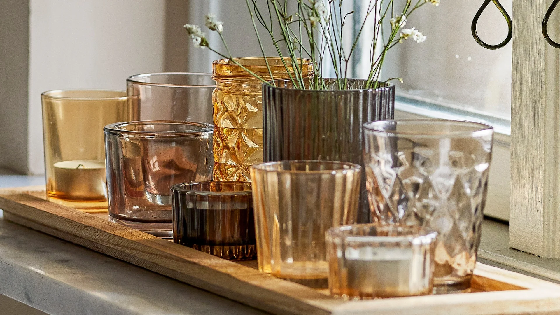 Die perfekte Boho Deko: Das Sanga Tablett mit Teelichthaltern in verschiedenen Gelb- und Brauntönen von Bloomingville steht auf einer Fensterbank.