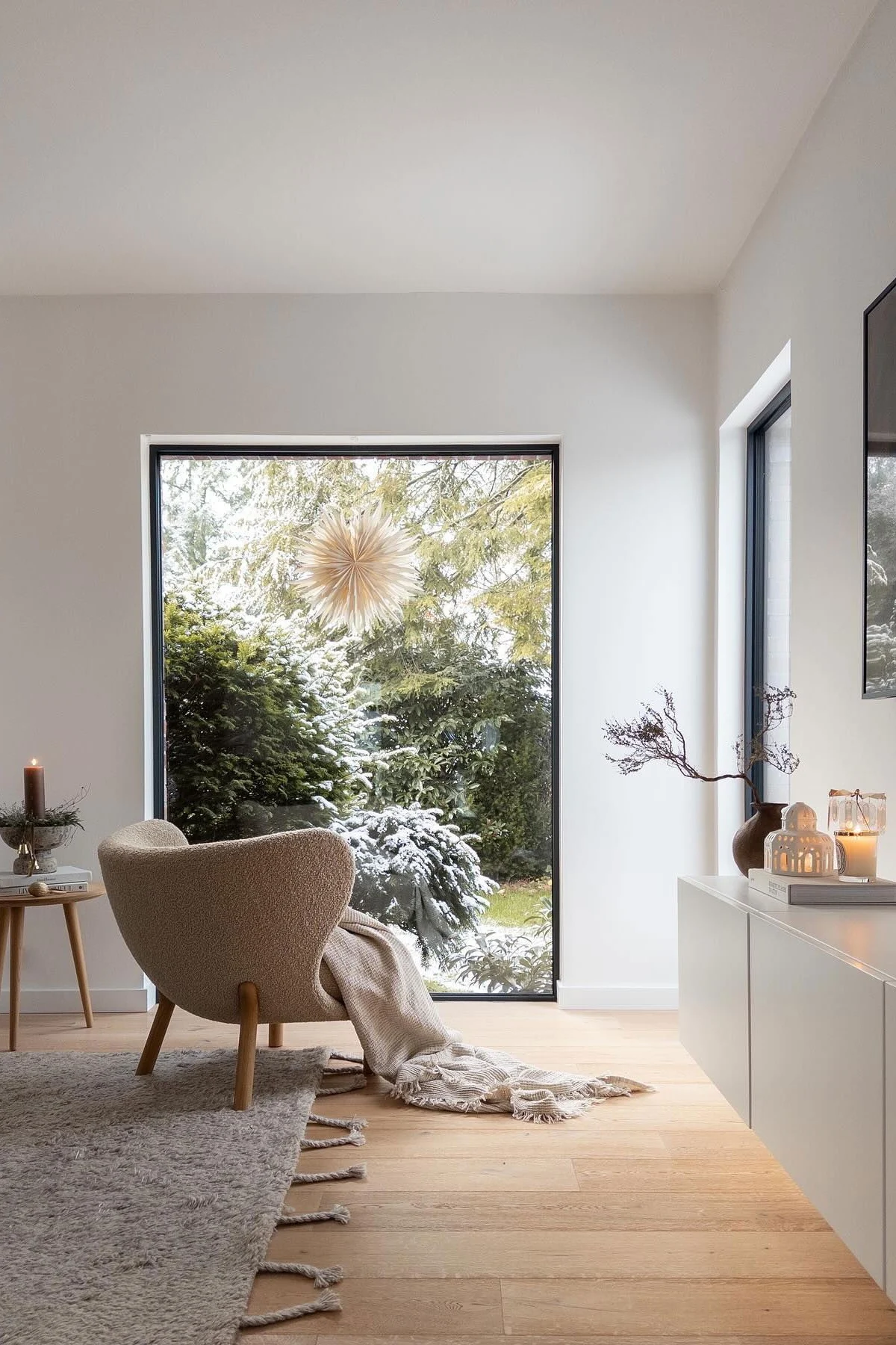 Ein Wohnzimmer mit sehr minimalistischer Weihnachtsdekoration. Am Fenster hängt ein Weihnachtsstern, daneben steht eine Kerze. 